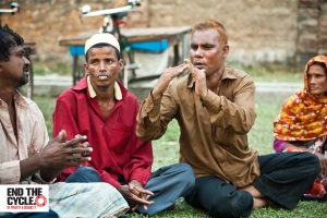 Picture of Waddud (third from left) two men and an older woman sitting on the grass outside using sign language to communicate.