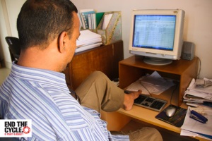 Picture of a man in Bangladesh sitting at a computer. He is using his left foot to operate the keyboard to his computer. 